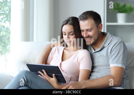Couple watching media on tablet sitting in a sofa at home Stock Photo