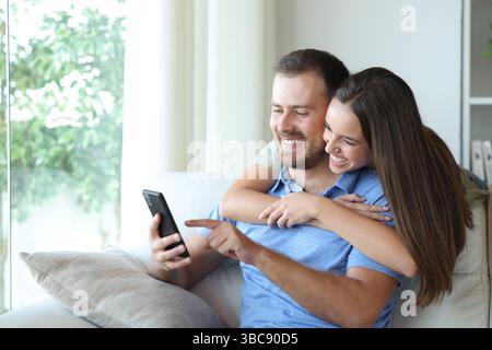Happy couple checking mobile phone content in a couch at home Stock Photo