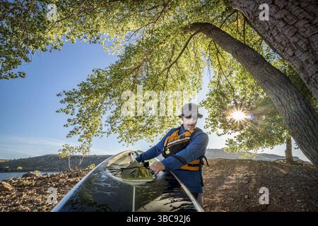 Senior male is carrying a stand up paddleboard on a shore of mountain lake, action camera POV Stock Photo