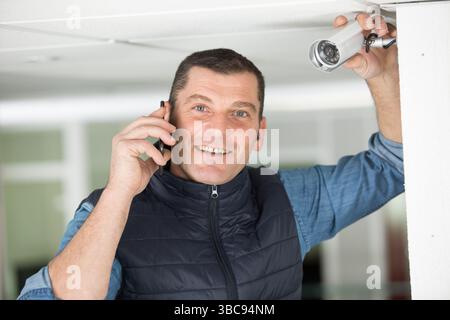 smiling contractor by cctv camera using smartphone Stock Photo