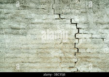 Damaged cracked old white brick wall structure, due to structural foundation failure and deterioration of building materials, as urban background Stock Photo