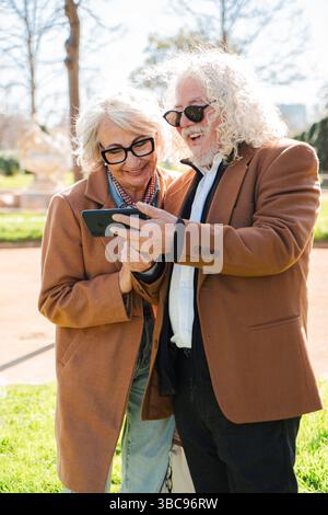 Delighted senior couple engaged in a joyful moment as they explore their smartphone, sharing smiles and laughter while discovering new applications Stock Photo