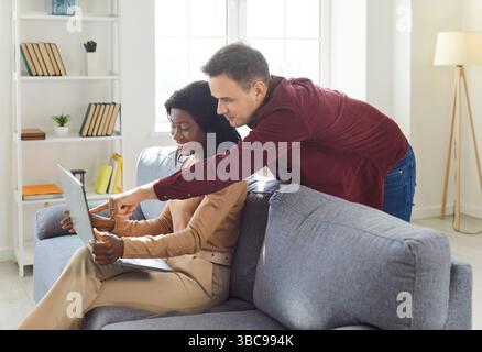 Multiracial young couple, interracial family at home using laptop online, african american woman Stock Photo