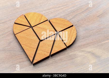 Heart version of tangram, a traditional Chinese Puzzle Game made of different wood parts to build abstract figures from them, on grained wood Stock Photo