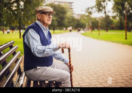 Portrait of lonely senior man in park. He is sitting on bench on autumn day. Stock Photo