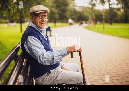 Portrait of happy senior man in park. He is sitting on bench and enjoying autumn day. Stock Photo