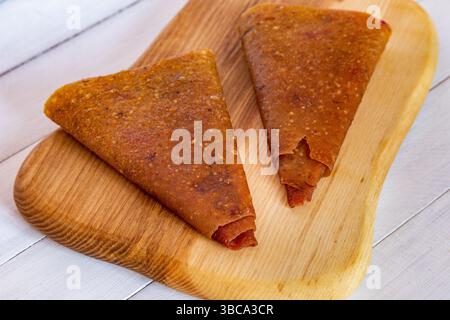 Close view of folded light brown triangular fruit pastille pieces on wooden cutting board showing rustic surface Stock Photo