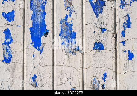 Cracked white wall with patches of peeling blue paint. Stock Photo