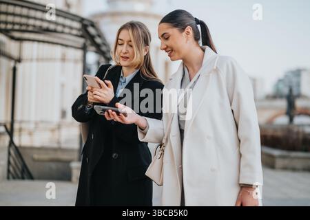 Two professional coworkers discussing work together while using mobile phones outdoors Stock Photo