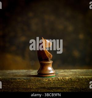 A beautifully crafted wooden chess knight piece stands prominently on a wooden surface. Stock Photo