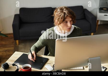 A young man engages in creative work at his desk, concentrating on a digital tablet while studying. Stock Photo