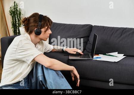 Focused young man engages in studying at home with headphones and school materials nearby. Stock Photo