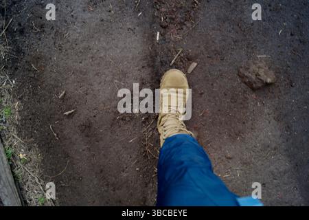 A single boot steps forward on a well-worn dirt trail, captured from a first-person perspective. The photo evokes themes of exploration & resilience. Stock Photo