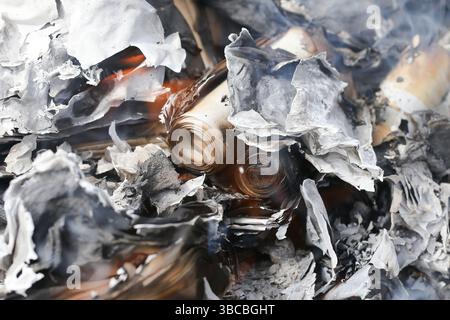 Burned newspapers and paper. Rolled pages turned into ashes. Fire destruction background. Charred texture and grey smoke. Aftermath of flame. Stock Photo