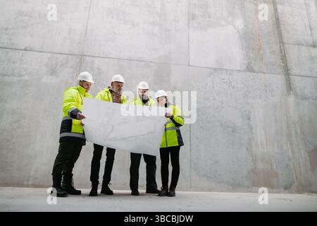Team of engineers and construction workers reviewing blueprints, building site. Stock Photo