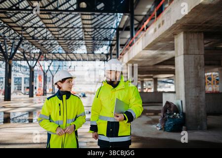 Engineers discussing construction plans using a tablet on site. Stock Photo