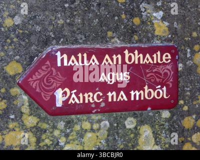 Rustic Irish Directional Signpost with Gaelic Text on a Weathered Wall. Gold Coast, Ireland Stock Photo