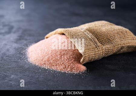 pink himalayan salt pours out of the bag on a black stone table, selective focus. Stock Photo