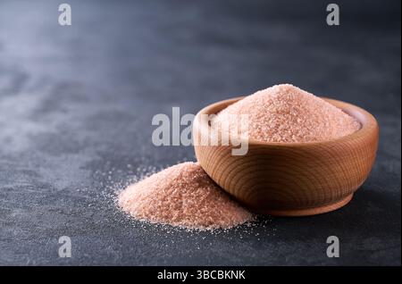 pink himalayan salt in a wooden bowl on a black stone table, selective focus. Stock Photo