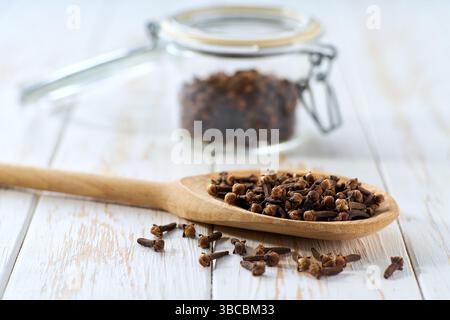 cloves spice in a wooden scoop and in glass storage jar on a white wooden table, selective focus. Stock Photo
