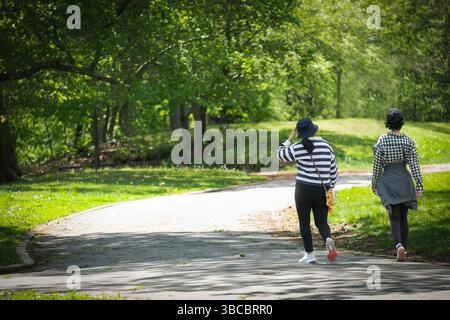 Two Chinese American women dressed in black & white walk on a windy path in Kissena Park on a sunny spring day. Stock Photo