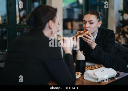 Two women enjoying pizza while having a casual conversation in a cozy cafe Stock Photo