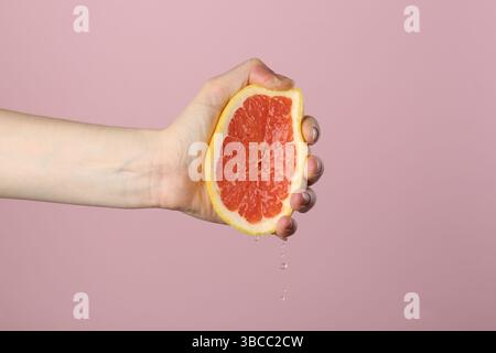 Woman squeezing grapefruit on pink background, closeup Stock Photo