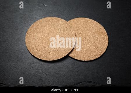 Blank cork beer coasters on black slate plate. Copy space for text. Selective focus. Stock Photo