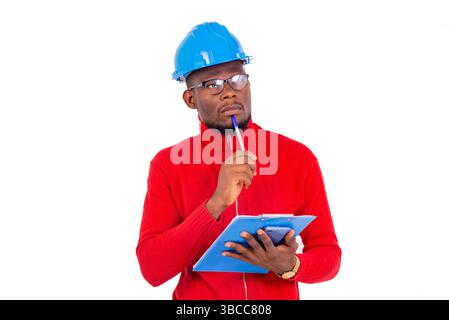 a man engineer wearing safety helmet standing on white background thinking while holding a notepad. Stock Photo