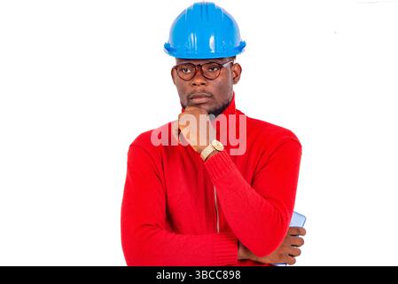 a young man with safety helmet standing on white background thinking with hand under chin. Stock Photo