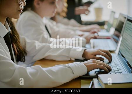 Group of students attentively using laptops in classroom setting, engaging with educational content on screens. Focus on collaborative learning experi Stock Photo
