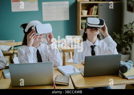 Students experiencing virtual reality in classroom setting while wearing headsets and interacting with laptops, demonstrating technology integration i Stock Photo