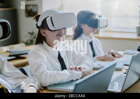 Students with VR headsets sitting in classroom, engaging in immersive technology. They appear focused and enthusiastic while experiencing virtual lear Stock Photo