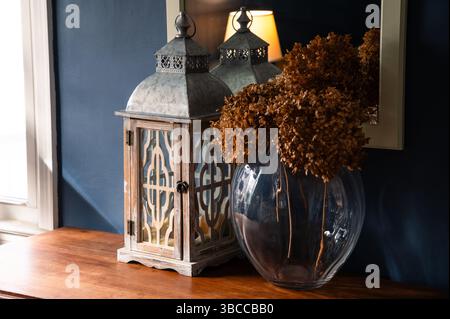 Dried hydrangea flowers and a white lantern on a wood console table in a blue room Stock Photo