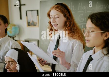 Group of students and nun engaged in academic presentation, with cross and blackboard in background, sharing knowledge in structured environment Stock Photo