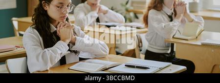 Students deeply focused on their studies in a bright classroom, with open books and notebooks placed on desks. Group studious environment emphasizes l Stock Photo
