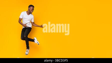 Guy Pointing Fingers Aside Having Fun Over Yellow Background, Panorama Stock Photo