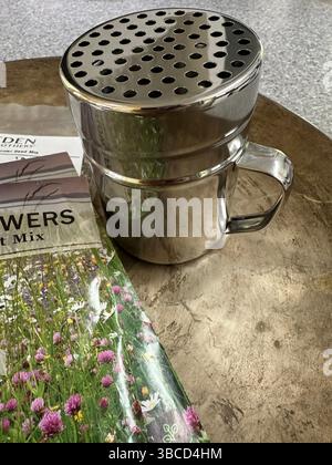 A metal shaker with large holes and packets of wildflower seeds, for spreading seeds. Stock Photo
