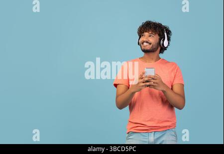 Happy eastern guy using wireless headset and smartphone, copy space Stock Photo
