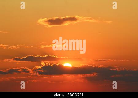 Stunning golden sunset with the sun partially hidden behind dramatic clouds, casting warm orange hues across the sky in a peaceful and serene atmosphe Stock Photo