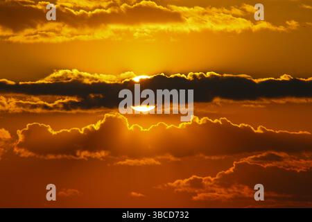 Stunning golden sunset with the sun partially hidden behind dramatic clouds, creating a warm and vivid sky perfect for nature and atmospheric themes. Stock Photo