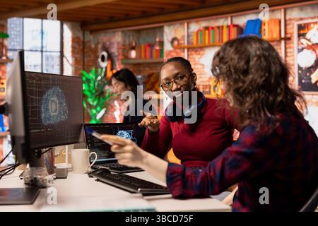 AI startup office colleagues cooperating, designing and implementing algorithms enabling machine learning. Teamworking artificial intelligence tech venture employees collaborating to fix code bugs Stock Photo