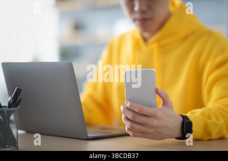 Asian man sitting at desk using cell phone Stock Photo
