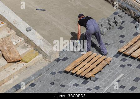 Lviv Ukraine 04.30.25 A construction worker is carefully placing stones for pavement at a building site. Wooden pallets rest beside the area, indicati Stock Photo