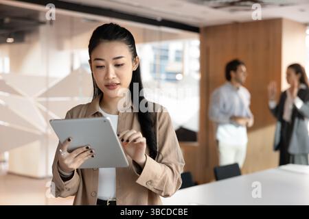Focused Vietnamese businesswoman working on tablet device standing in boardroom Stock Photo