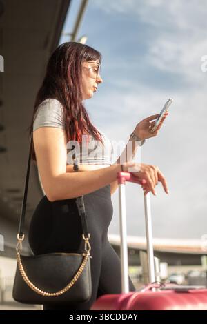 Young woman using smartphone while waiting at airport with luggage Stock Photo