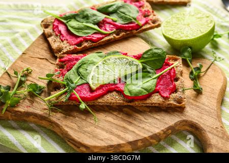 Wooden board with tasty crispbreads, beetroot hummus and basil on table, closeup Stock Photo
