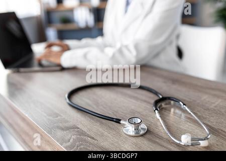 Stethoscope and background doctor using laptop at desk in clinic working on computer at office, cropped Stock Photo