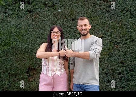 Young couple fist bumping celebrating success in front of hedge Stock Photo