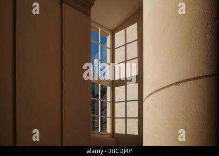 Sunlight streams through a multi-pane window, casting geometric shadows onto a smooth, beige interior wall. Stock Photo